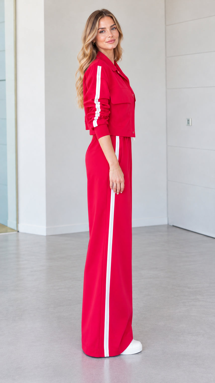 Side profile view of woman wearing red 2-piece track set with white side stripes
