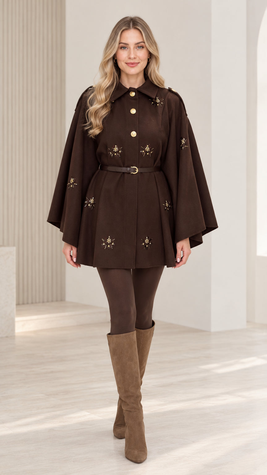 Front view of woman wearing chocolate brown embellished belted cape coat with tall boots