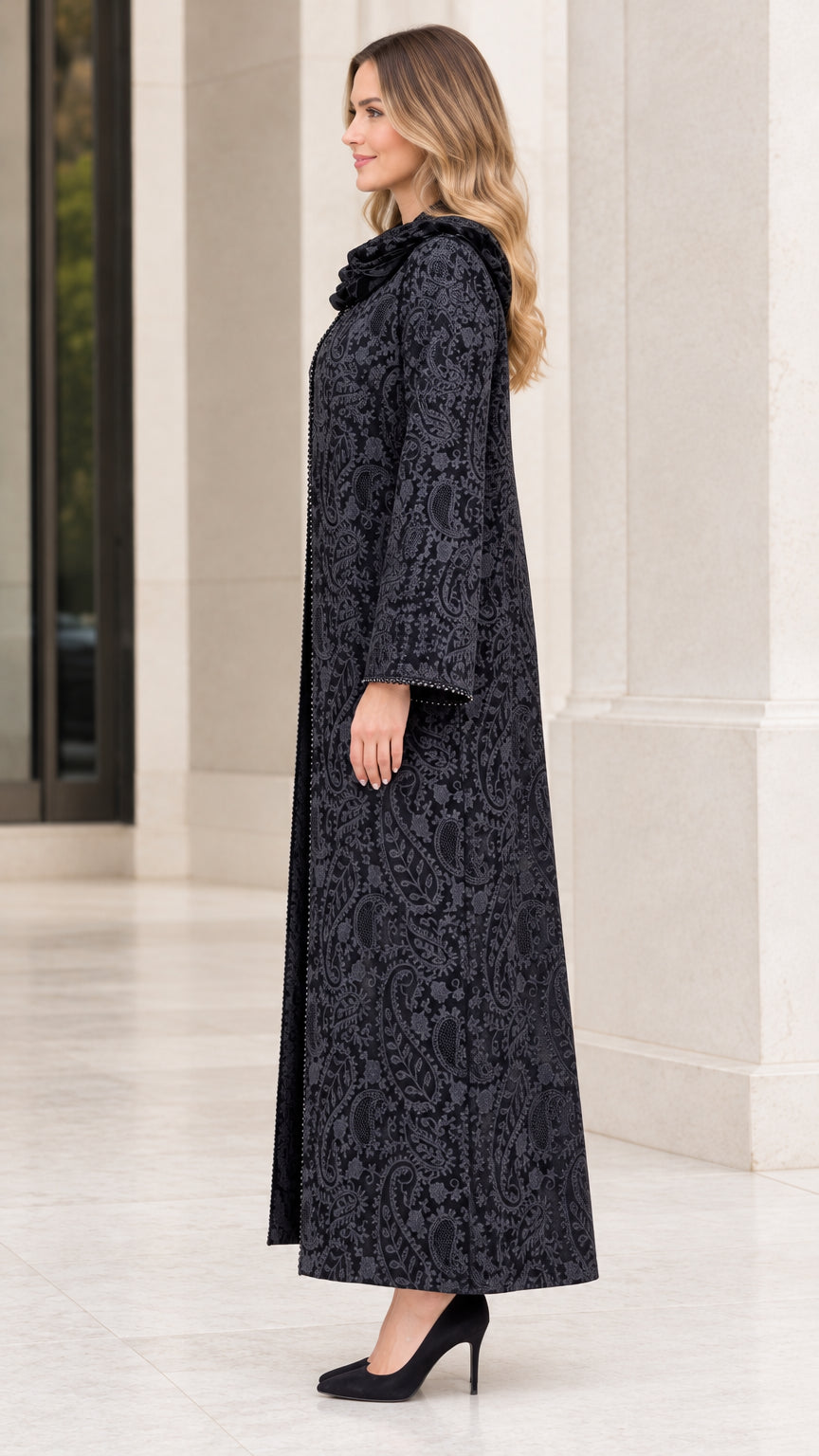 Side profile view of woman wearing black paisley jacquard maxi duster coat with beaded accents