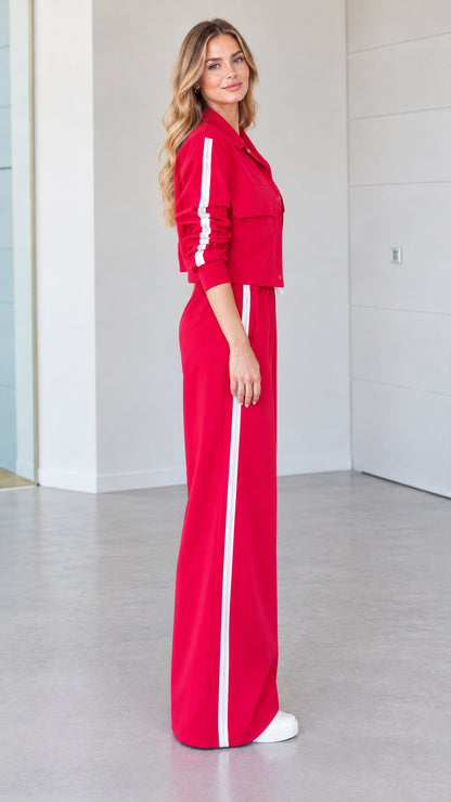 Side profile view of woman wearing red 2-piece track set with white side stripes