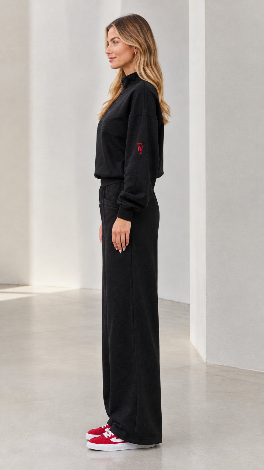 Side profile view of woman wearing black matching tracksuit set with red sneakers