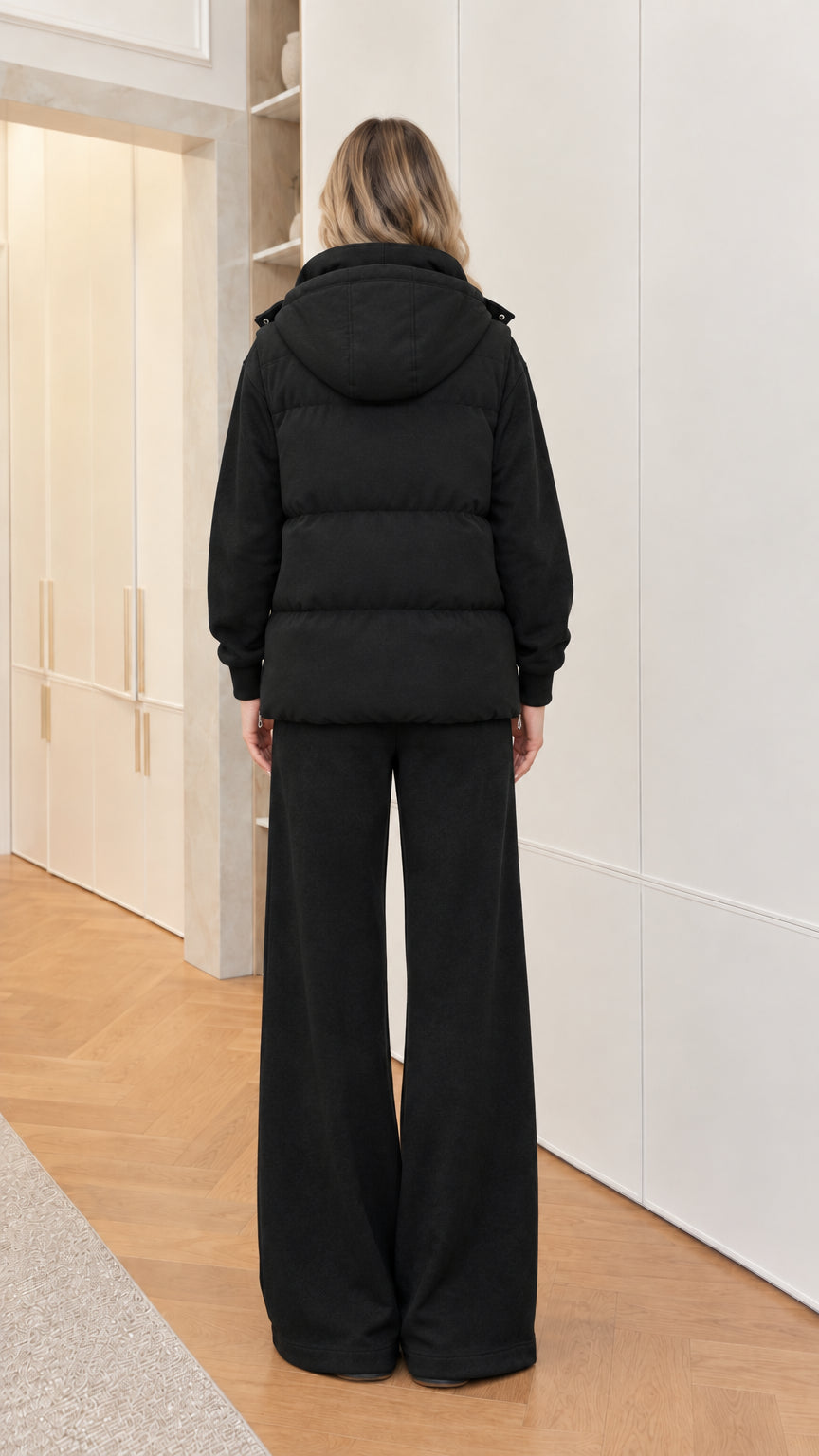 Back view of woman wearing black hooded puffer vest and wide-leg pants