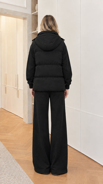 Back view of woman wearing black hooded puffer vest and wide-leg pants