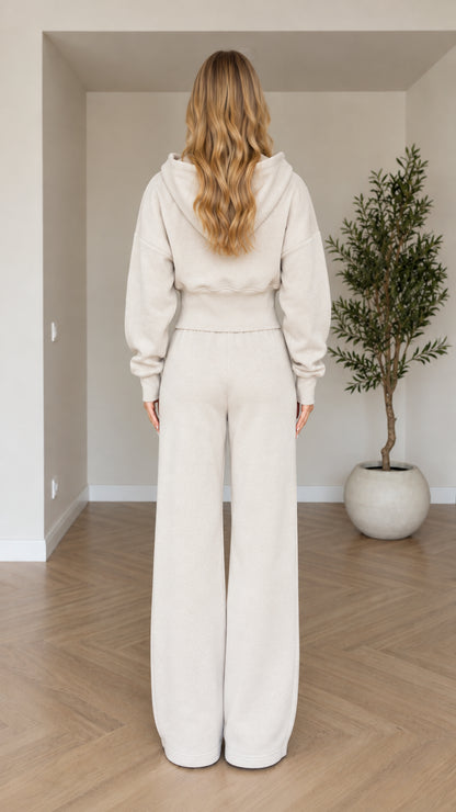 Back view of woman wearing beige cropped hoodie and wide-leg track pants