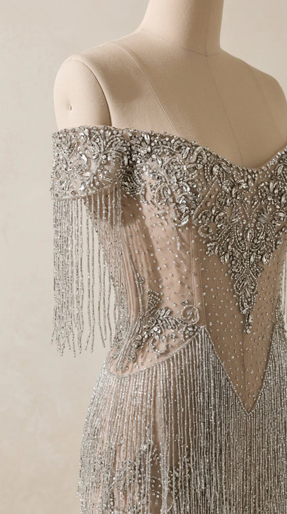 Close-up detail of silver crystal beading, illusion mesh, and draped fringe sleeves