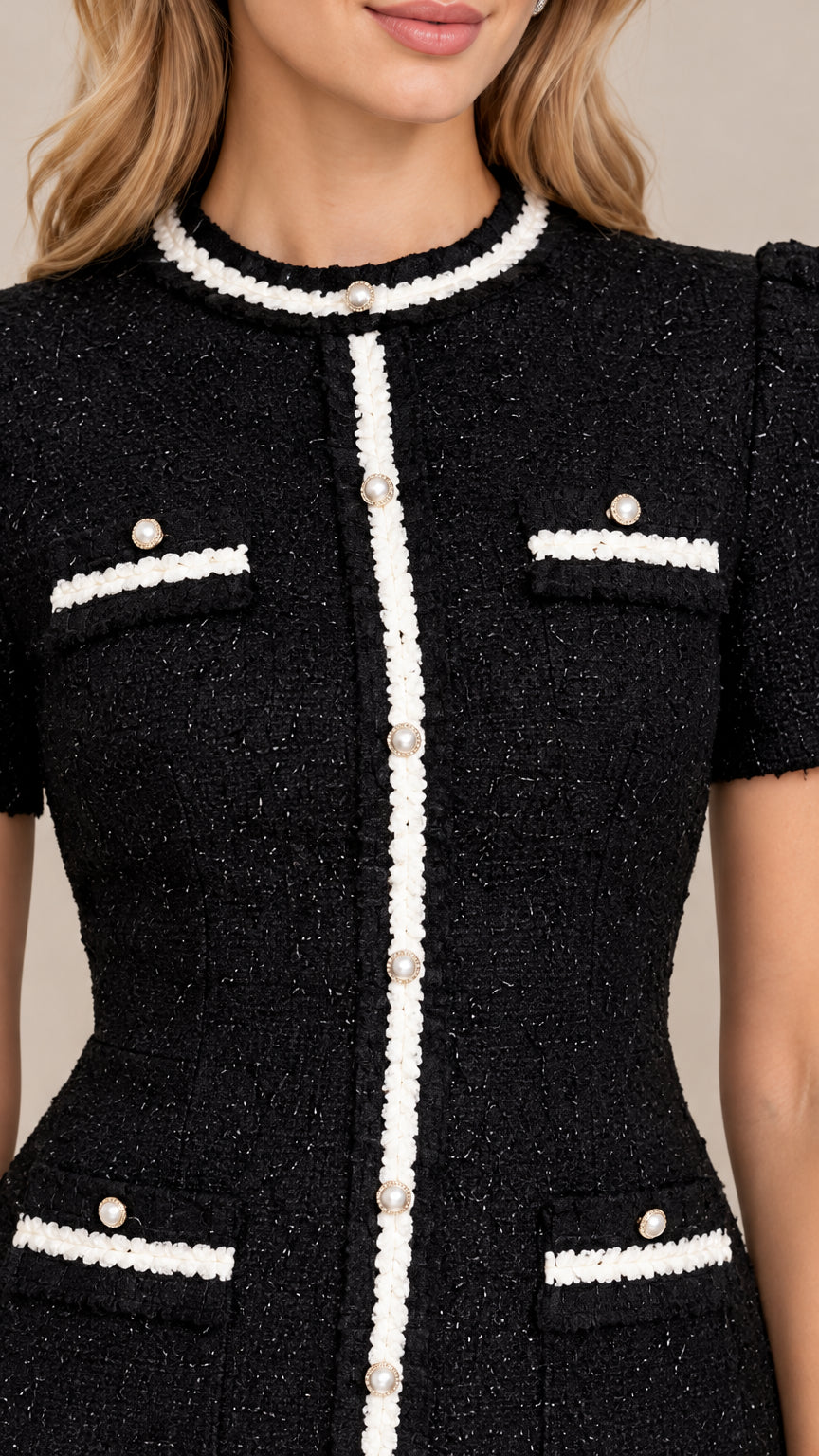 Close-up detail of textured black tweed fabric, white braided trim, and faux pearl buttons